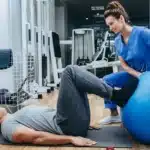 Physical therapist helps patient perform an exercise with feet on a large inflated ball